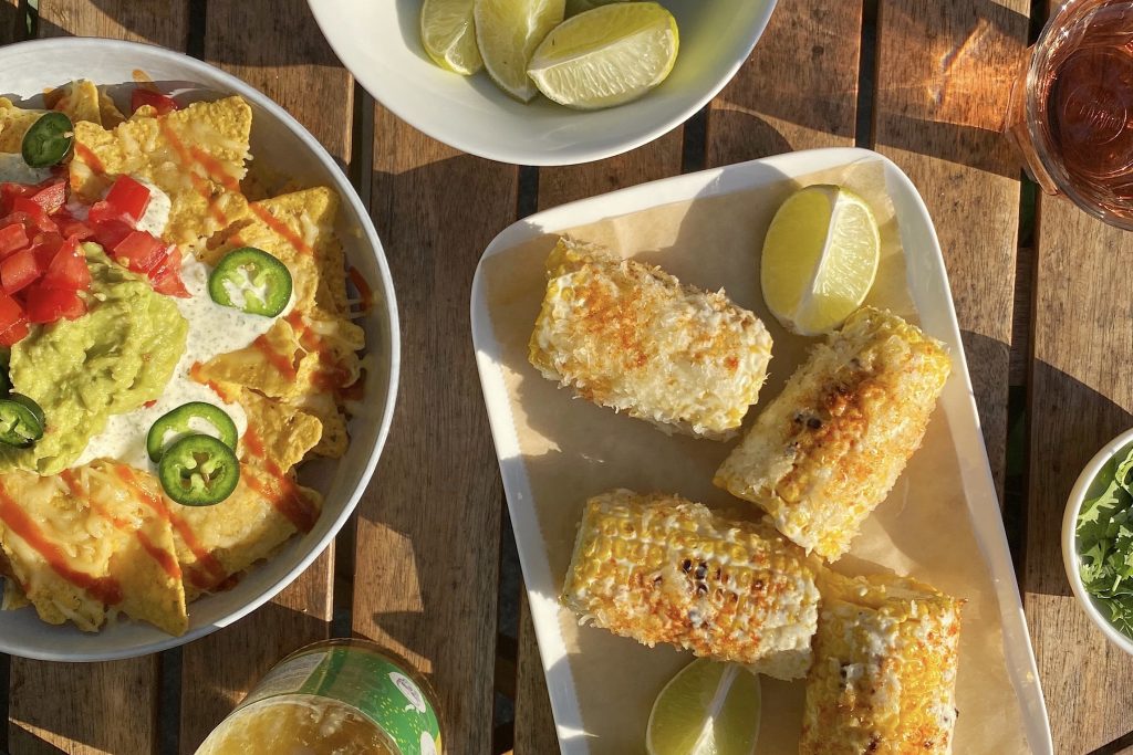 mexican corn elote on table with nachos and limes